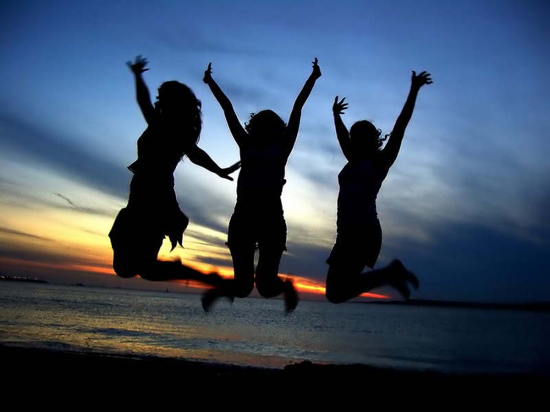 Three girls in silhouette jumping on beach in celebration