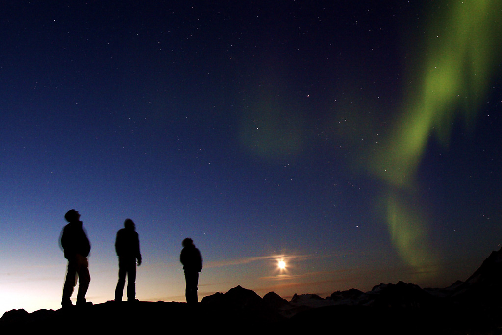 Three travelers watching the Northern Lights in Greenland